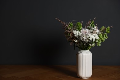 Photo of Beautiful flowers in vase on wooden table against dark grey background, space for text
