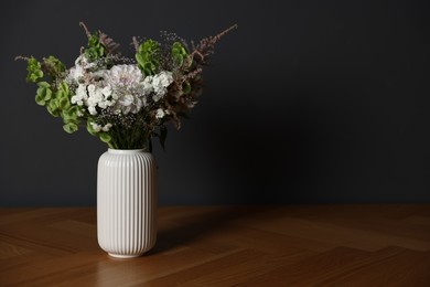 Photo of Beautiful flowers in vase on wooden table against dark grey background, space for text