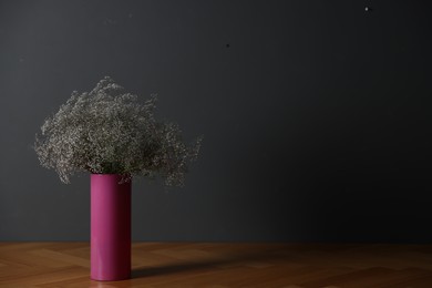 Photo of Beautiful flowers in vase on wooden table against dark grey background, space for text