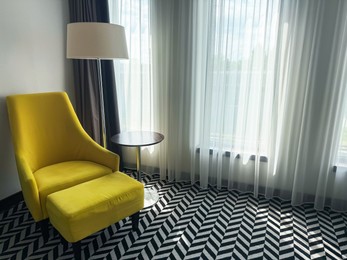 Photo of Yellow armchair, pouf, lamp and side table near window indoors. Interior design
