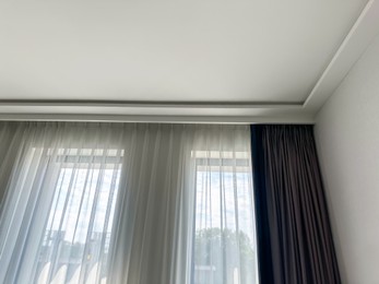 Photo of Beautiful curtains hanging on cornice near window indoors, low angle view