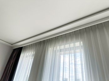 Photo of Beautiful curtains hanging on cornice near window indoors, low angle view