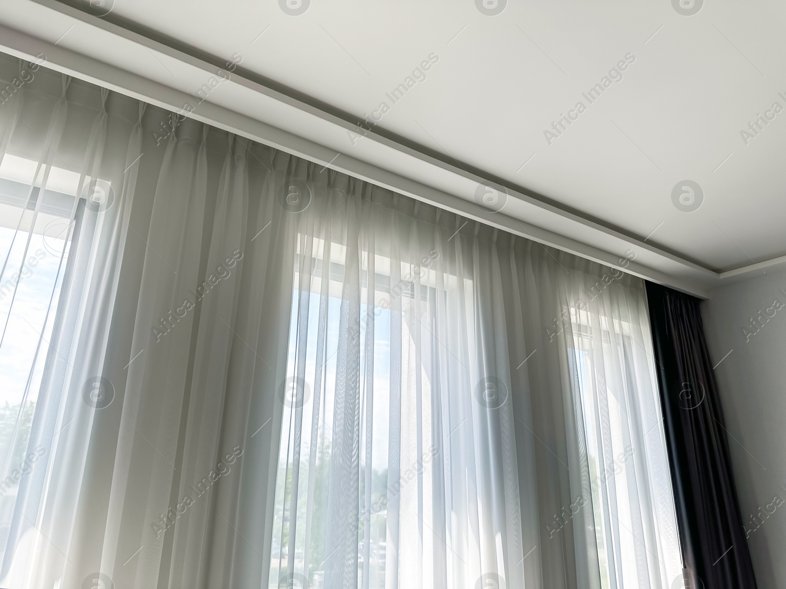 Beautiful curtains hanging on cornice near window indoors, low angle view Photo of Beautiful curtains hanging on cornice near window indoors, low angle view