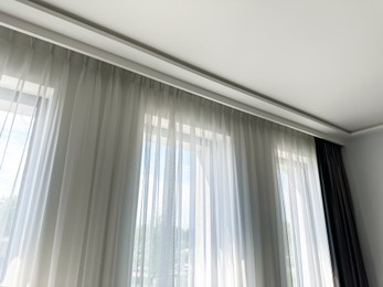 Photo of Beautiful curtains hanging on cornice near window indoors, low angle view