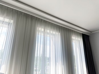 Photo of Beautiful curtains hanging on cornice near window indoors, low angle view