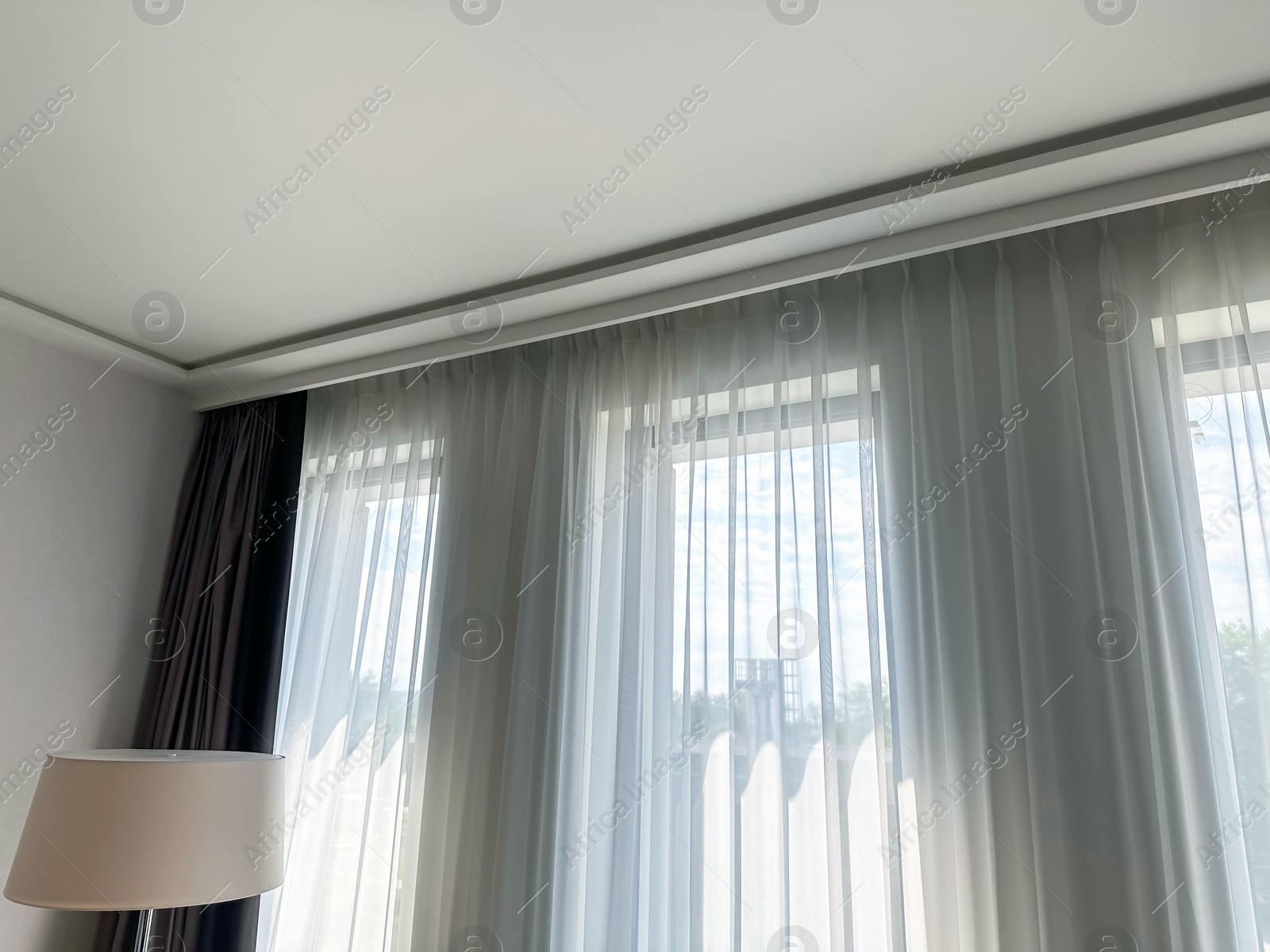 Beautiful curtains hanging on cornice near window indoors, low angle view Photo of Beautiful curtains hanging on cornice near window indoors, low angle view