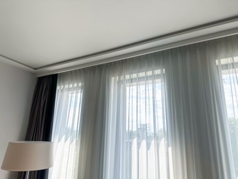 Photo of Beautiful curtains hanging on cornice near window indoors, low angle view