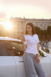 Photo of Beautiful woman with smartphone near modern car outdoors on sunny day