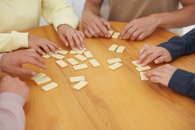 Photo of Friends playing dominoes at wooden table, closeup