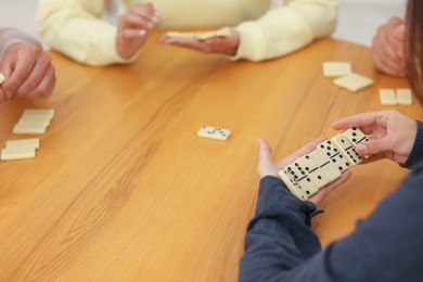 Photo of Friends playing dominoes at wooden table, closeup