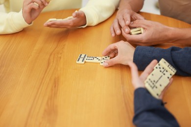 Photo of Friends playing dominoes at wooden table, closeup