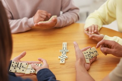Photo of Friends playing dominoes at wooden table, closeup