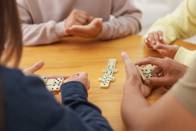 Photo of Friends playing dominoes at wooden table, closeup