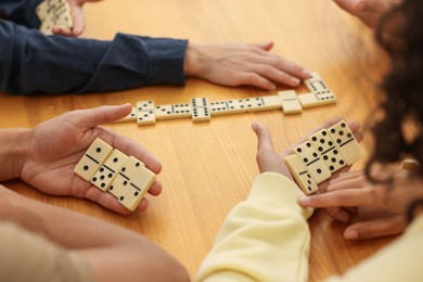 Photo of Friends playing dominoes at wooden table, closeup