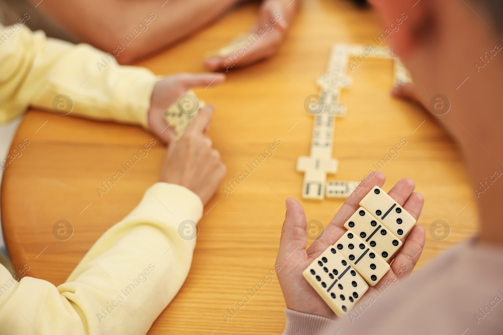 Friends playing dominoes at wooden table, closeup Photo of Friends playing dominoes at wooden table, closeup