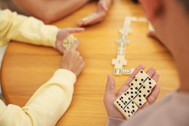 Photo of Friends playing dominoes at wooden table, closeup
