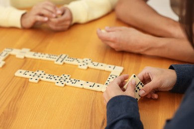Photo of Friends playing dominoes at wooden table, closeup