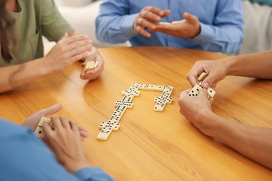 Photo of Friends playing dominoes at wooden table indoors, closeup