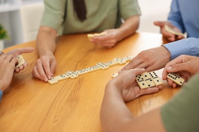 Photo of Friends playing dominoes at wooden table indoors, closeup