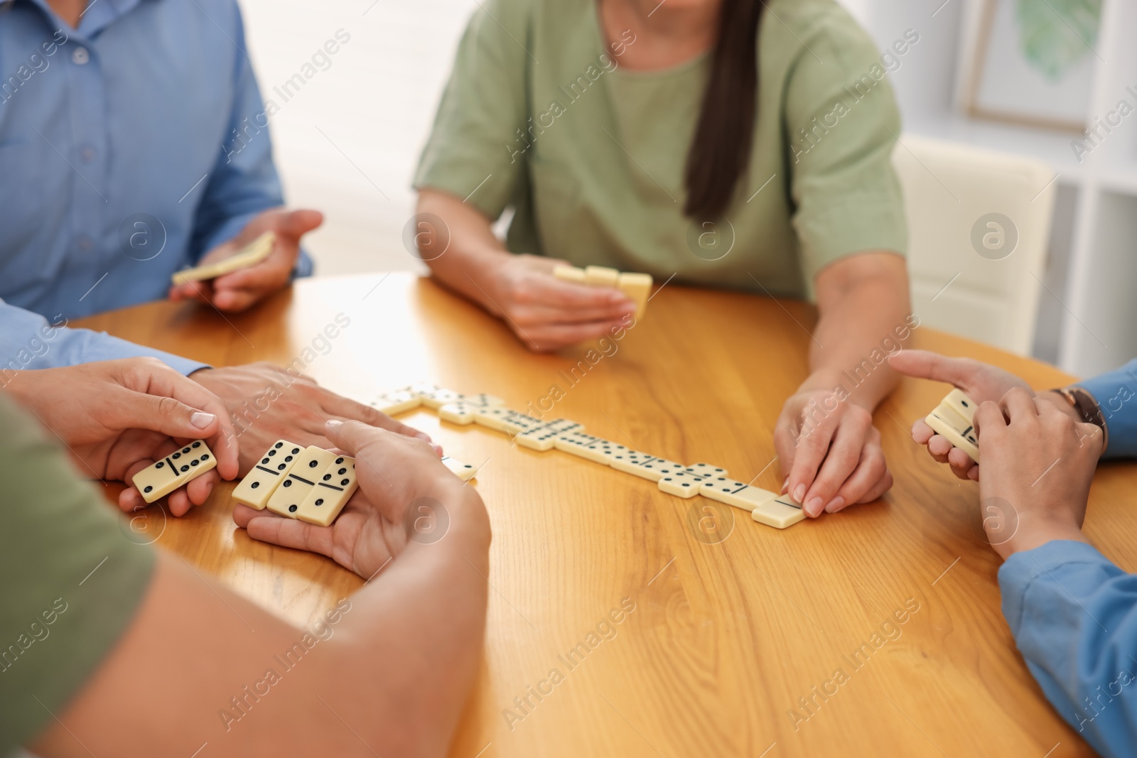 Friends playing dominoes at wooden table indoors, closeup Photo of Friends playing dominoes at wooden table indoors, closeup