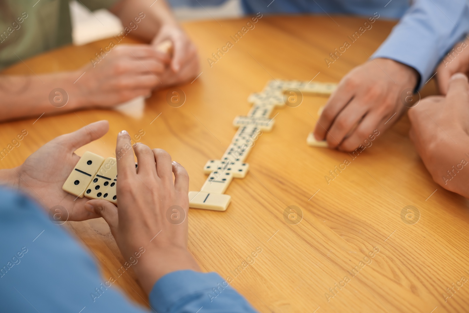 Friends playing dominoes at wooden table, closeup Photo of Friends playing dominoes at wooden table, closeup