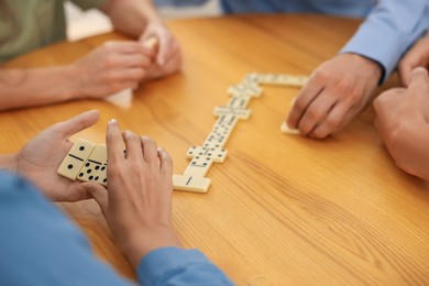 Photo of Friends playing dominoes at wooden table, closeup