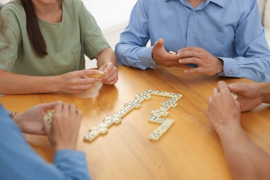 Photo of Friends playing dominoes at wooden table against light background, closeup