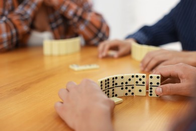 Photo of friends playing dominoes at wooden table against light background, closeup