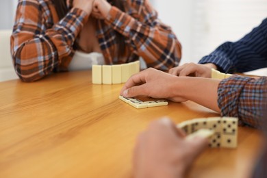 Photo of friends playing dominoes at wooden table against light background, closeup