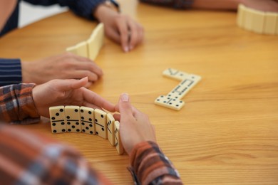Photo of Friends playing dominoes at wooden table, closeup