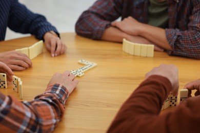 Photo of Friends playing dominoes at wooden table, closeup