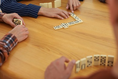 Photo of Friends playing dominoes at wooden table, closeup