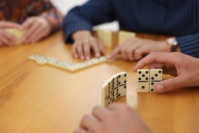 Photo of Friends playing dominoes at wooden table, closeup