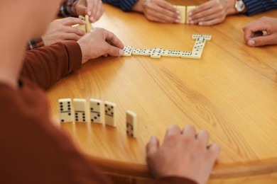Photo of Friends playing dominoes at wooden table, closeup