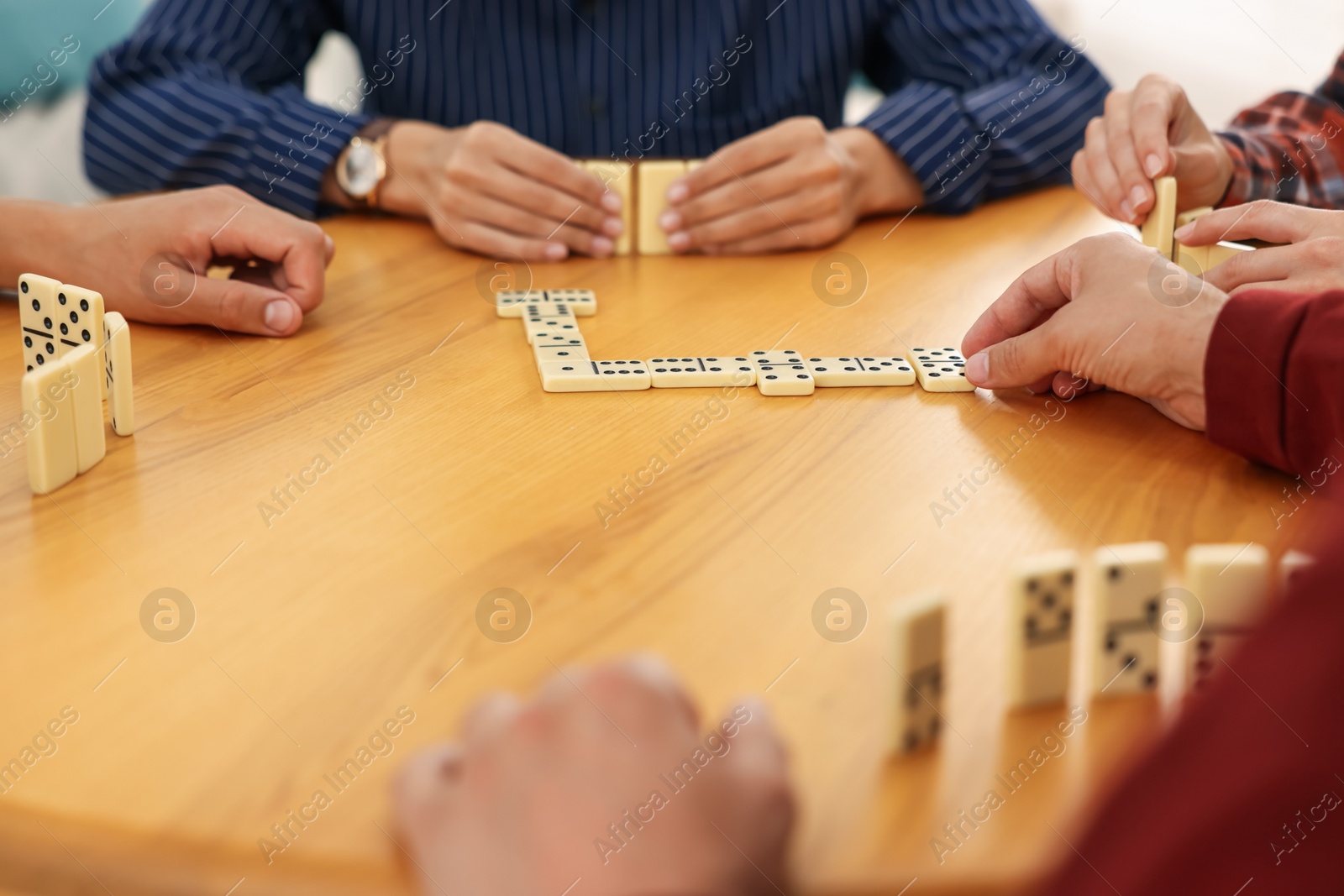 Friends playing dominoes at wooden table, closeup Photo of Friends playing dominoes at wooden table, closeup