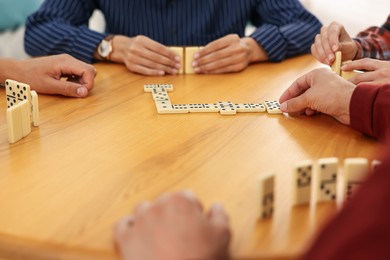 Photo of Friends playing dominoes at wooden table, closeup