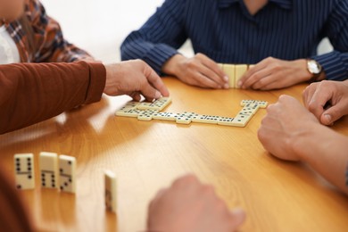 Photo of Friends playing dominoes at wooden table against light background, closeup