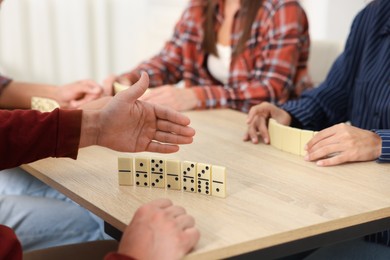 Photo of Friends playing dominoes at light wooden table indoors, closeup