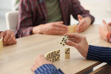 Photo of Friends playing dominoes at light wooden table, closeup