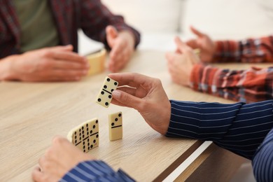 Photo of Friends playing dominoes at light wooden table, closeup