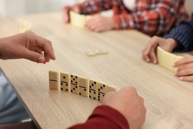 Photo of Friends playing dominoes at light wooden table, closeup
