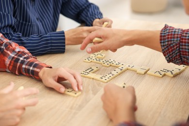 Photo of Friends playing dominoes at light wooden table, closeup