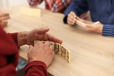 Photo of Friends playing dominoes at light wooden table, closeup