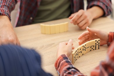 Photo of Friends playing dominoes at light wooden table, closeup