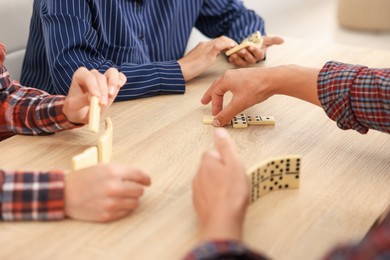Photo of Friends playing dominoes at light wooden table, closeup