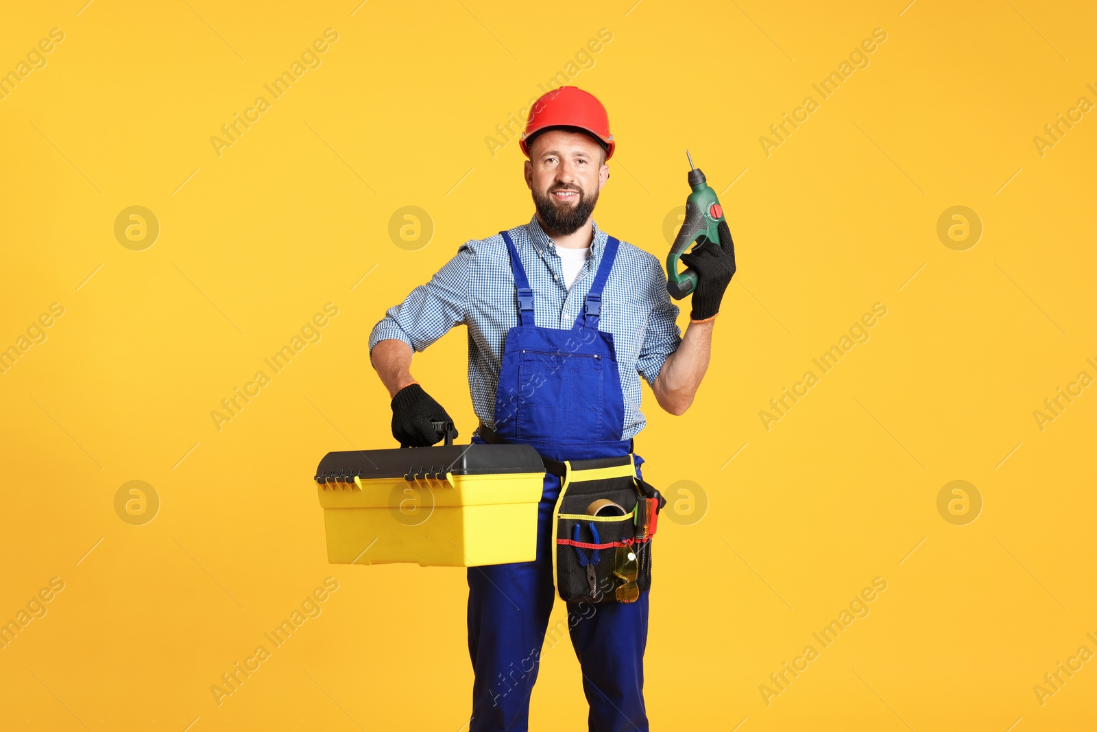 Professional repairman with tool box and electric screwdriver on orange background Photo of Professional repairman with tool box and electric screwdriver on orange background