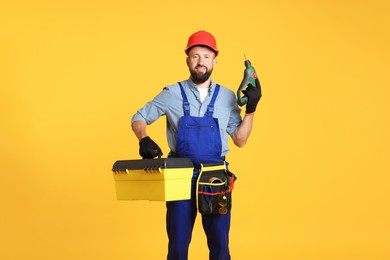 Photo of Professional repairman with tool box and electric screwdriver on orange background