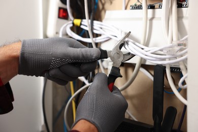 Photo of Man fixing heating radiator with pliers indoors, closeup