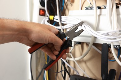 Photo of Man fixing heating radiator with pliers indoors, closeup
