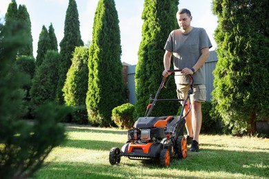 Photo of Man cutting green grass with lawn mower in garden